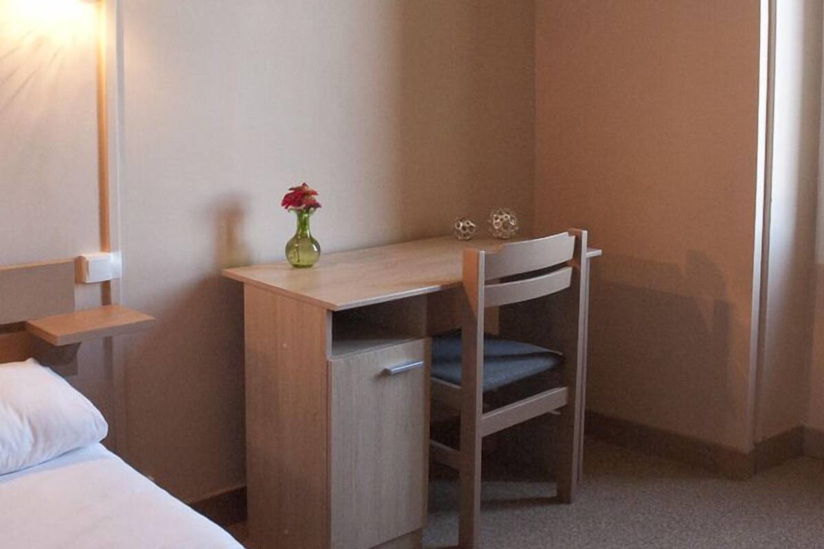 Une petite pièce, de taille modeste, comprenant un lit, un bureau et une chaise.