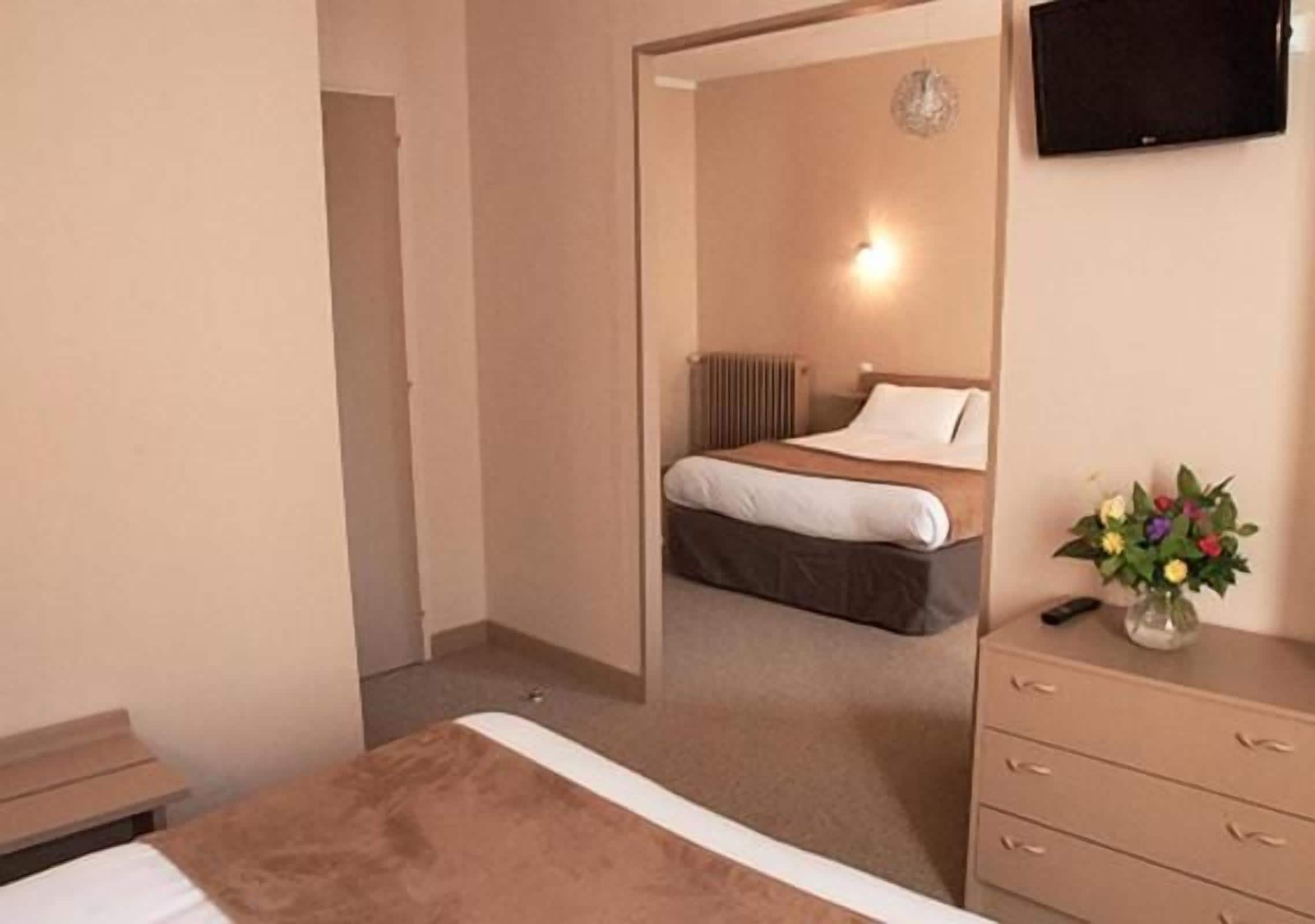 A hotel room with a bed, a dresser, a television, and a vase with flowers.