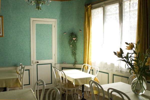 Un área de comedor con una mesa, sillas, una puerta y un ventanal con cortinas.