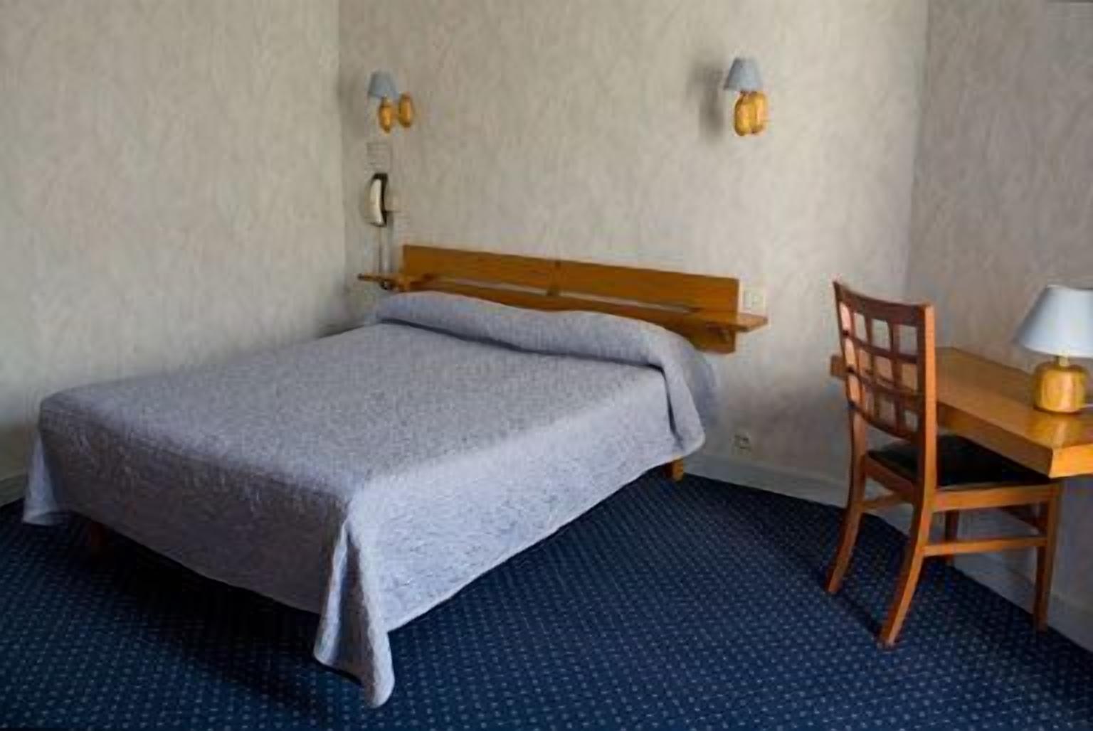 Un dormitorio con cama, escritorio, silla y dos lámparas fijadas a la pared.