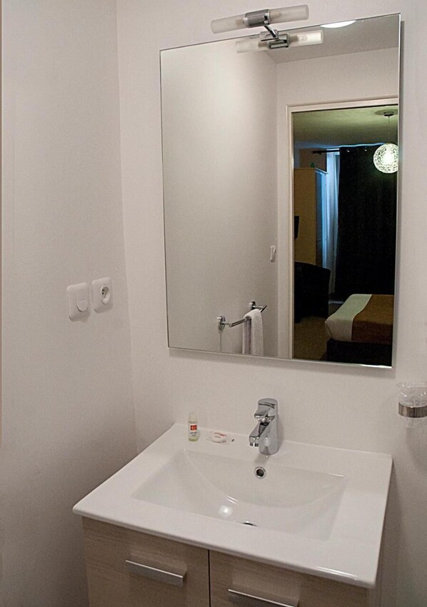 A bathroom with a white sink, a mirror, and a towel rack. - Hôtel des Pyrénées (Angouleme)