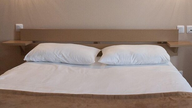 A hotel room with a bed, two pillows, a headboard, and wall-mounted lights.