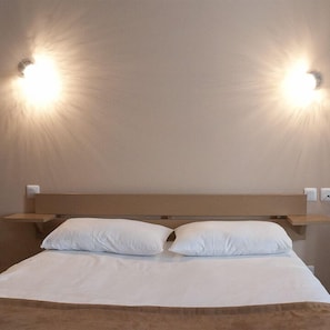 A hotel room with a bed, two pillows, a headboard, and wall-mounted lights. - Hôtel des Pyrénées (Angouleme)
