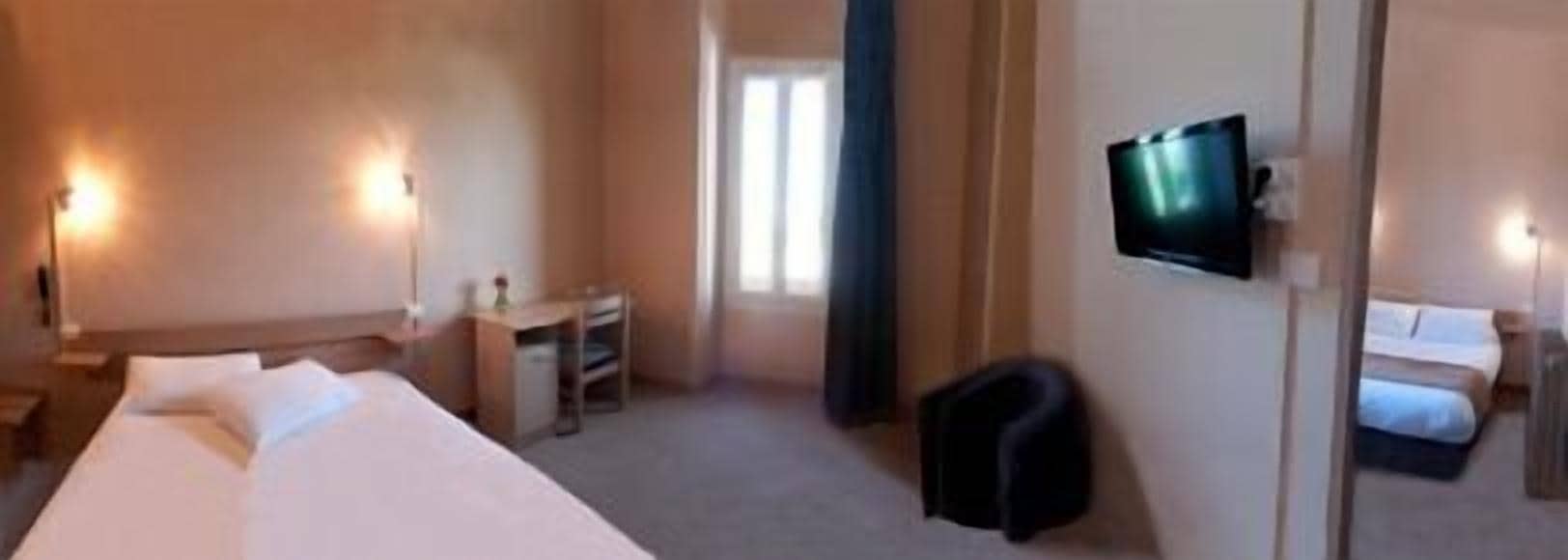 A hotel room with a bed, a desk, a chair, a TV, and a window.