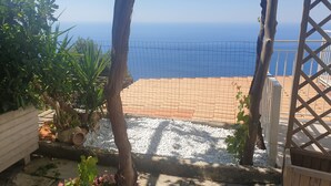 Une terrasse avec vue sur la mer, entourée de plantes et d’une clôture en bois.