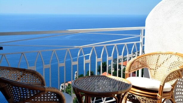 Un balcon avec des fauteuils en osier et une petite table, offrant une vue sur la côte.