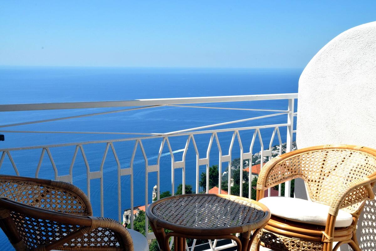 Ein Balkon mit Korbstühlen und einem kleinen Tisch mit Blick auf die Küste.