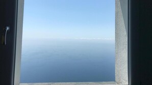 Une fenêtre donnant sur une mer calme et un ciel dégagé.