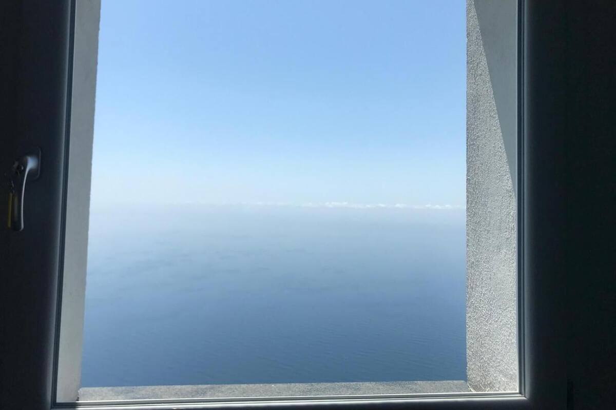 Ein Fenster mit Blick auf ein ruhiges Meer und einen klaren Himmel.