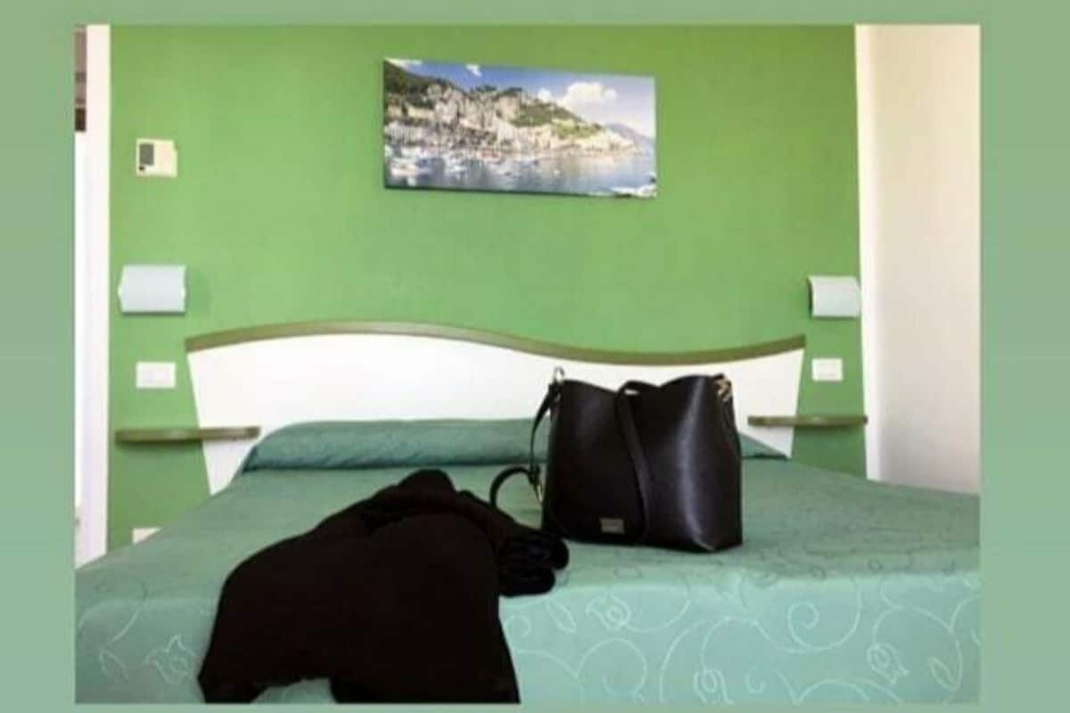 Ein Bett mit einem grünen Kopfteil, eine schwarze Jacke darauf und eine schwarze Handtasche daneben.