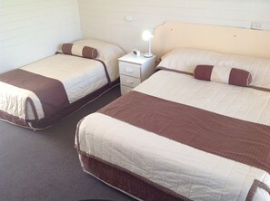 Two single beds with brown and white bedding, a nightstand with a lamp, and a white brick wall. - Sunraysia Motel & Holiday Apartments (Mildura)