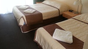 A hotel room with two beds, each with a brown and white quilt, a nightstand with a lamp, and a window with curtains. - Sunraysia Motel & Holiday Apartments (Mildura)
