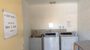 A laundry area with a sign indicating guest laundry is open daily from 8:00 AM to 8:00 PM. - Sunraysia Motel & Holiday Apartments (Mildura)