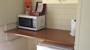 A compact kitchenette with a microwave, a small refrigerator, a trash bin, and a shelf with a box and papers. - Sunraysia Motel & Holiday Apartments (Mildura)