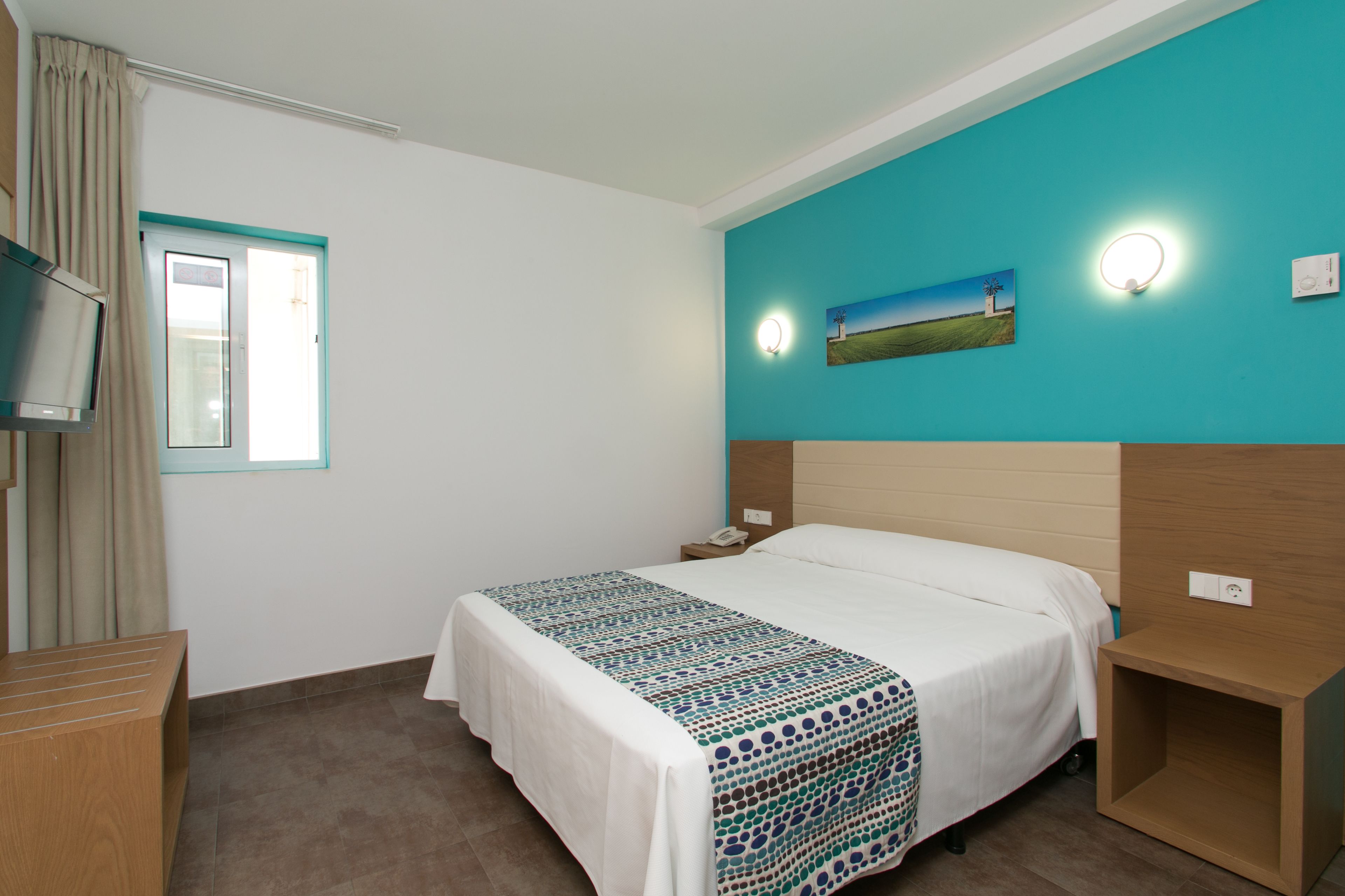 A hotel room with a bed, a bedside table, a TV, and a window with curtains.