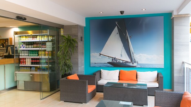 Un espace de détente moderne, comprenant un coin salon, un réfrigérateur pour les boissons et un grand tableau représentant un voilier accroché au mur.