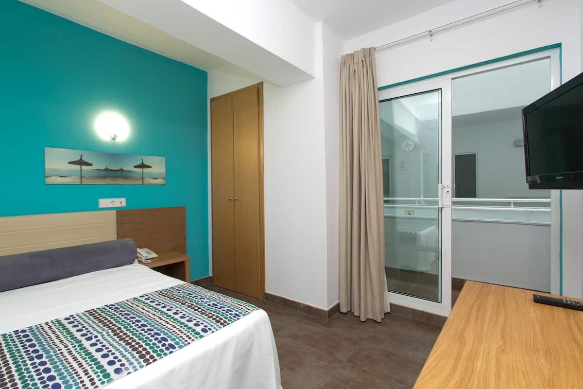 Quarto de hotel com cama, escrivaninha, televisão, porta de vidro deslizante e um quadro na parede.