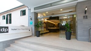 L’entrée de l’hôtel Don Pepe Mallorca, avec un comptoir d’accueil, des plantes en pot et un escalier menant à l’entrée principale.