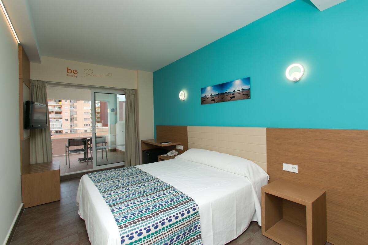 Quarto de hotel com cama, escrivaninha, televisão e vista para a varanda.
