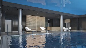 Piscina interior moderna con agua cristalina, rodeada de sillones de descanso y una pared de listones de madera.
