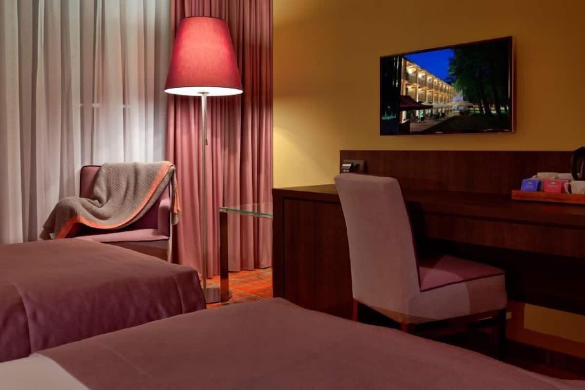 Ein Hotelzimmer mit zwei Betten, einem Schreibtisch, einem Sessel, einem Fernseher und einer Lampe.