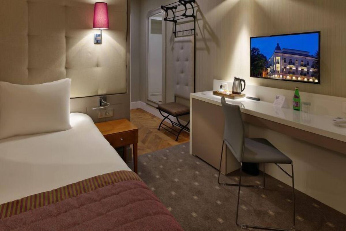 Ein Hotelzimmer mit Bett, Schreibtisch, Stuhl, Fernseher und Fenster mit Blick auf ein Gebäude.