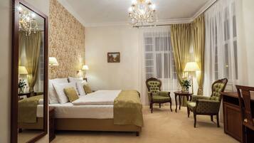 Habitación de hotel con una cama grande, dos sillones, un escritorio, una araña y un espejo amplio.