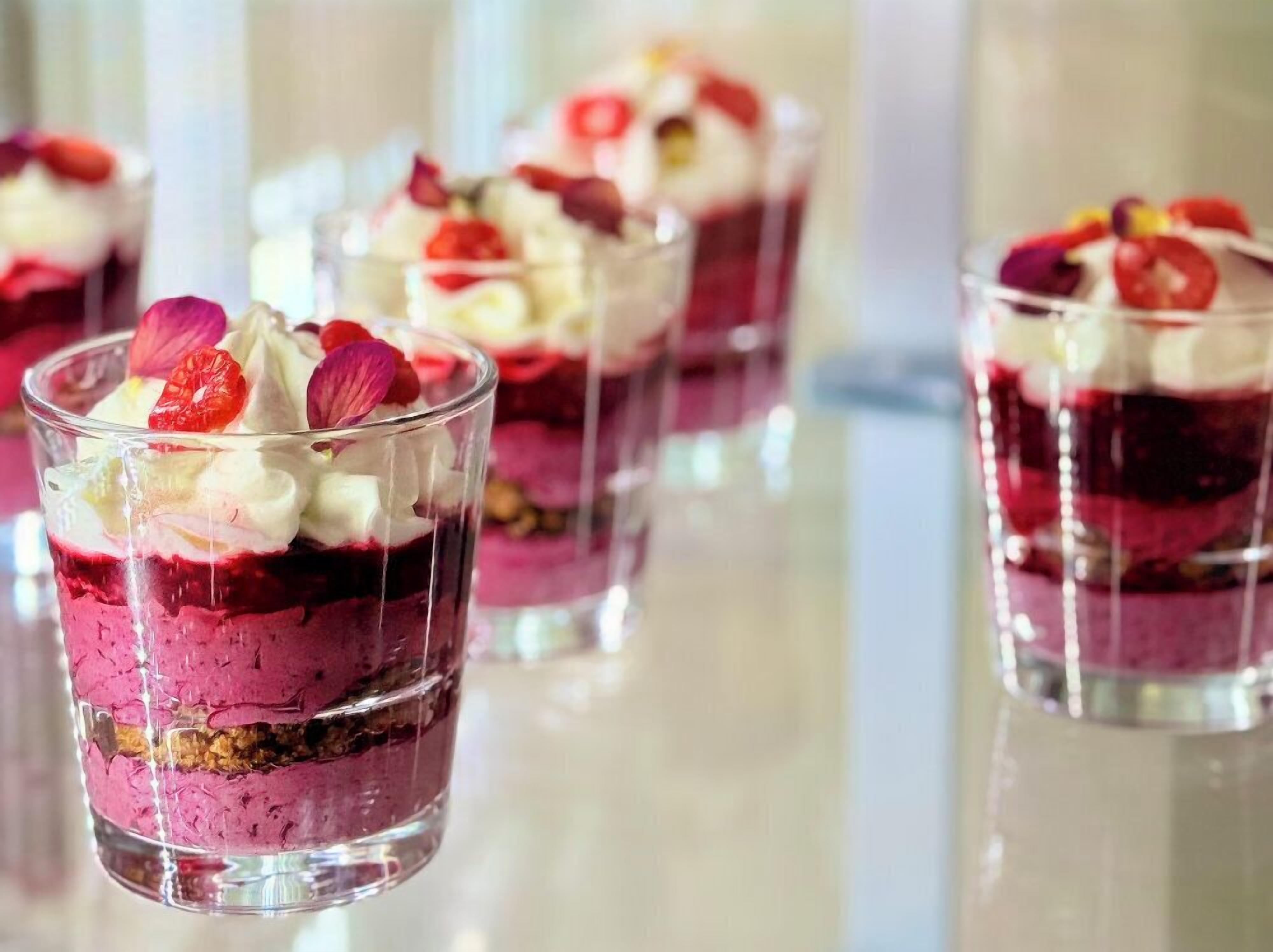 Un dessert con strati di gelatina rossa, crema bianca e una base friabile, decorato con frutta e fiori.