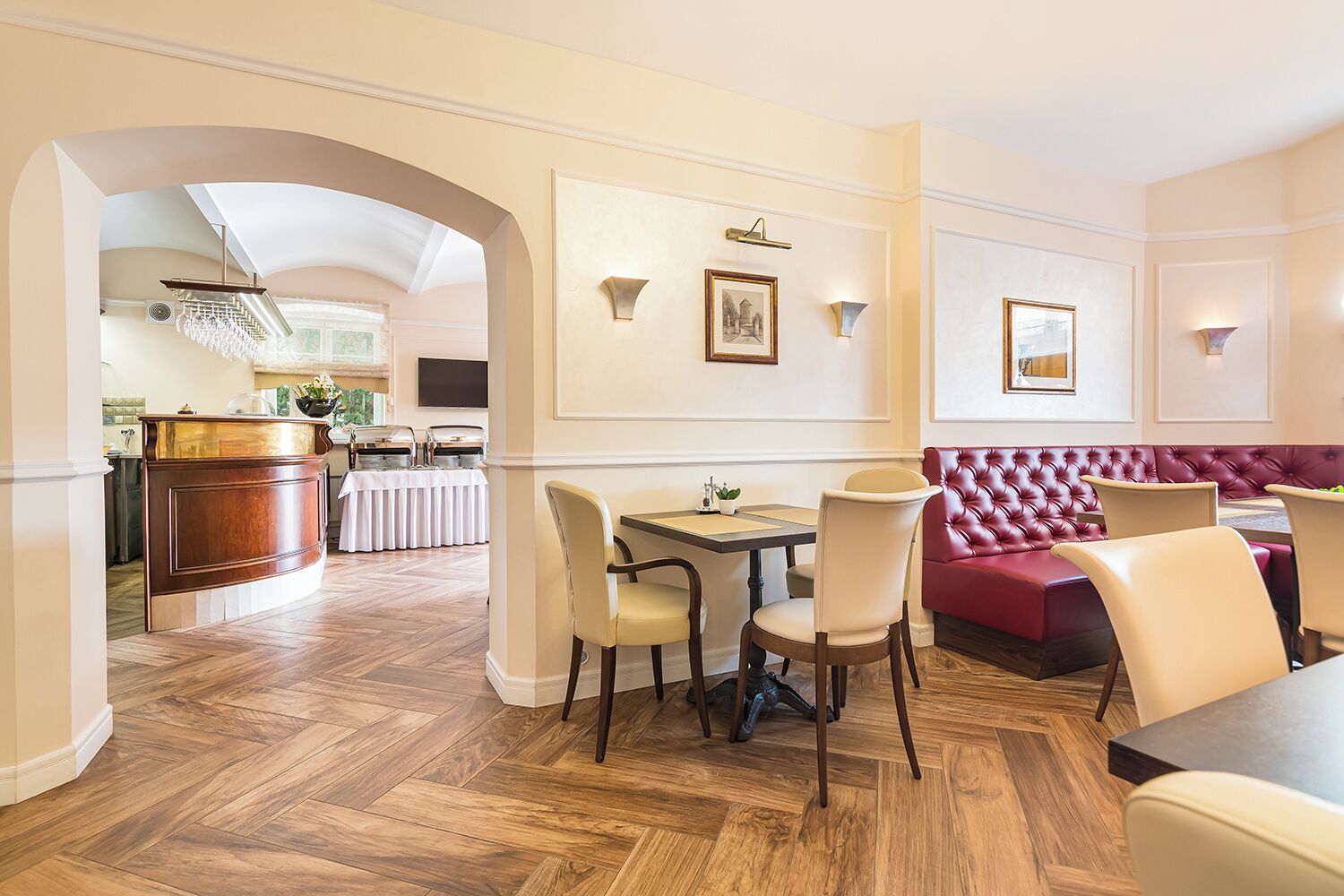 A dining area with a wooden herringbone floor, a buffet station, and a red upholstered bench.
