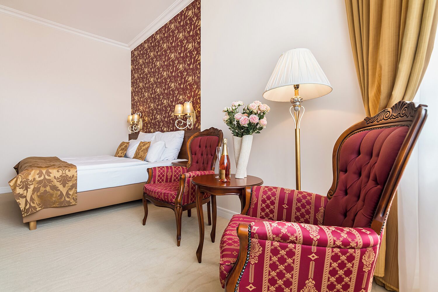 A hotel room with a bed, a sitting area with a chair and a table, a floor lamp, and a decorative wall panel.