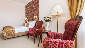 A hotel room with a bed, a sitting area with a chair and a table, a floor lamp, and a decorative wall panel.