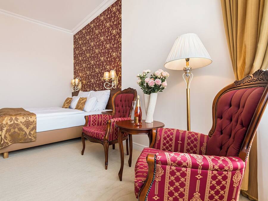 A hotel room with a bed, a sitting area with a chair and a table, a floor lamp, and a decorative wall panel.