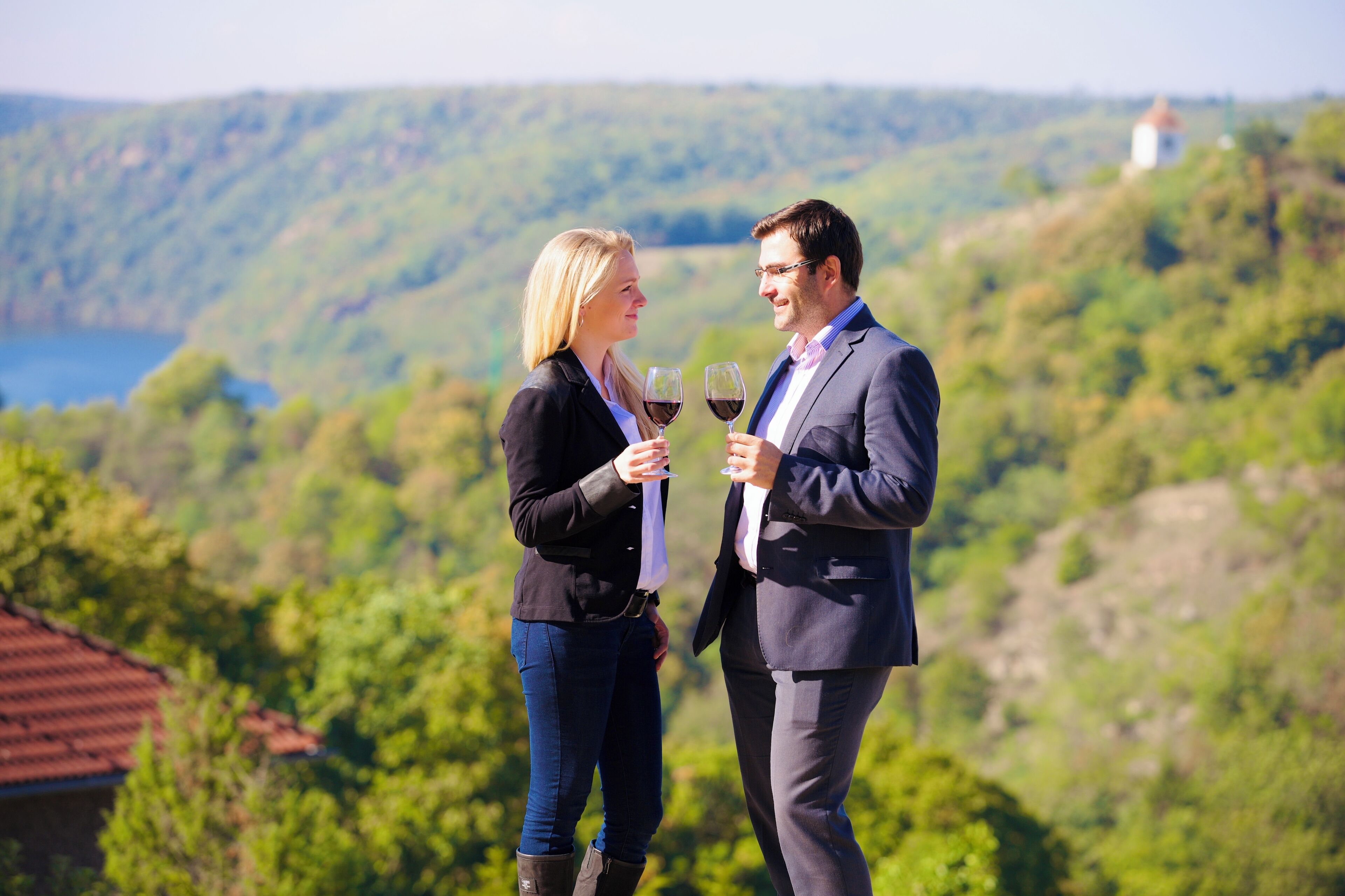 A couple standing on a hill overlooking a scenic landscape with a body of water and a lighthouse in the distance.