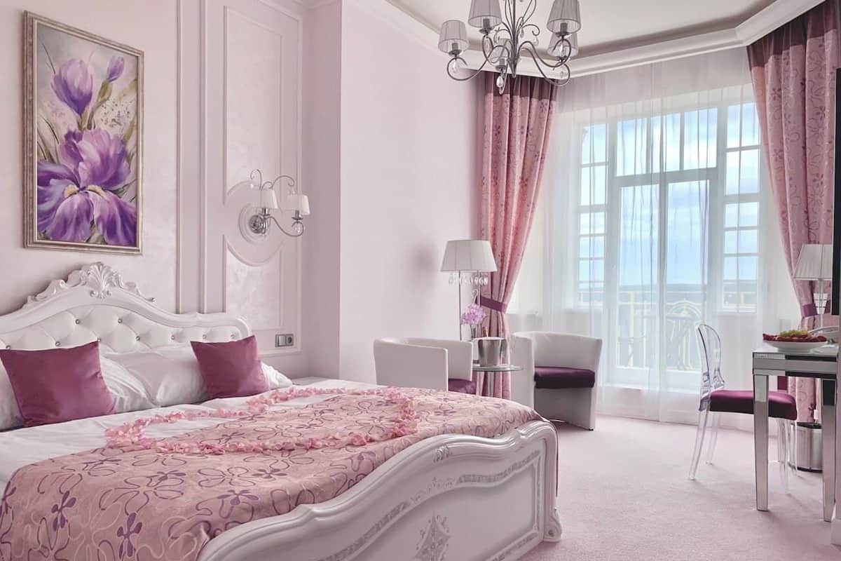 A bedroom with a large bed, a chandelier, a desk, and a chair.