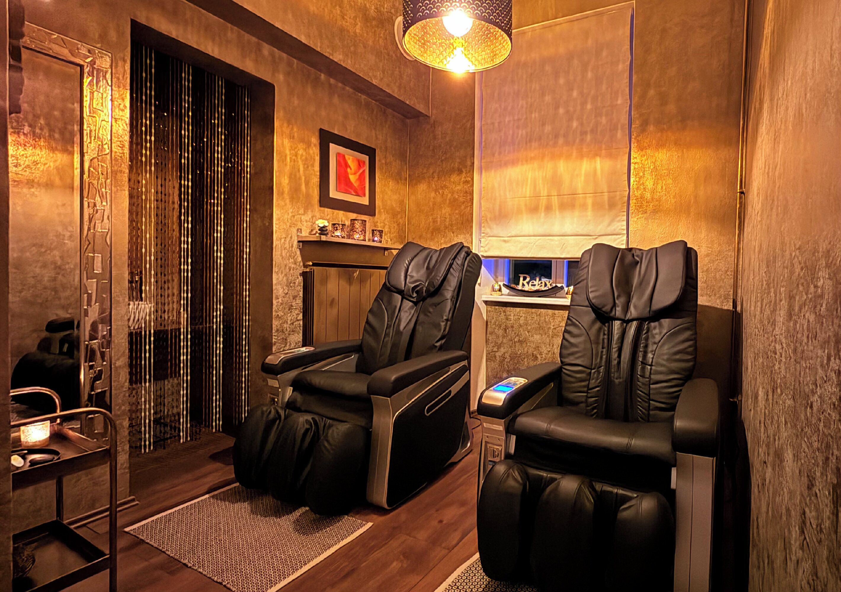 A room with two massage chairs, a small table, a mirror, and a wall-mounted massage table.