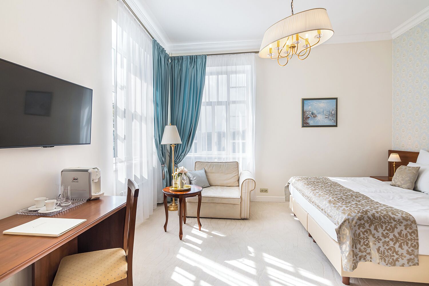 Habitación de hotel con cama, escritorio con cafetera, silla, televisor y ventana con cortinas.