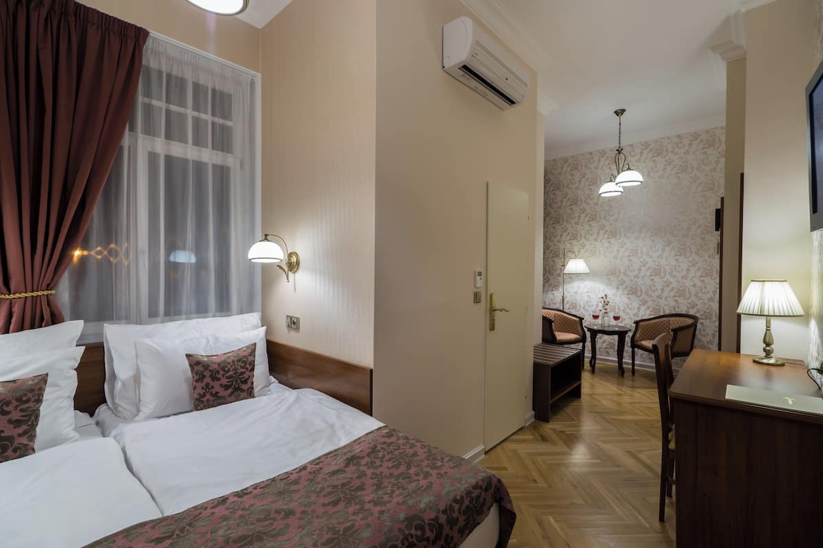 A hotel room with a bed, a desk, a chair, and a small table with a lamp.