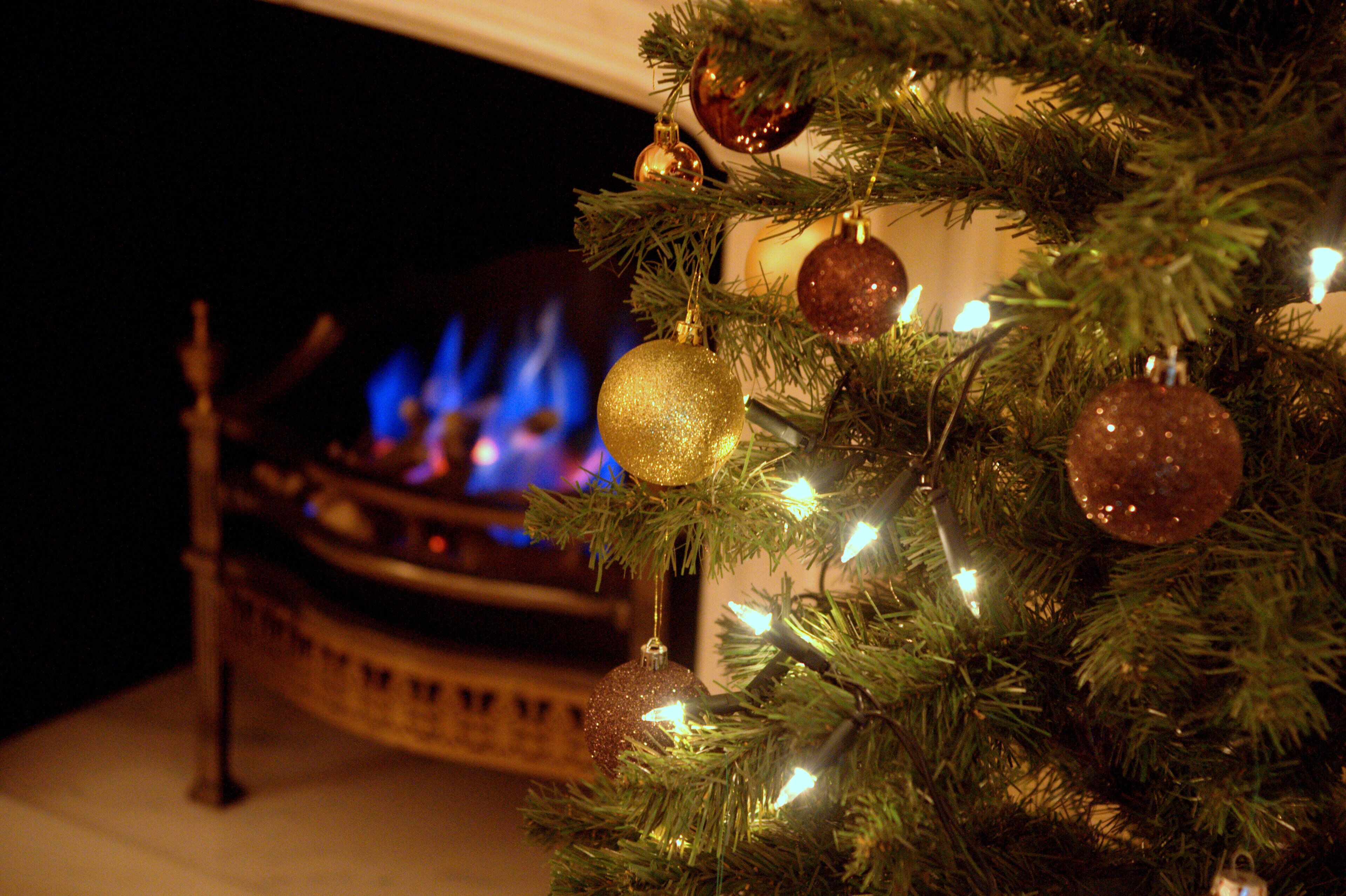 A Christmas tree with ornaments and a fireplace with a lit fire in the background.