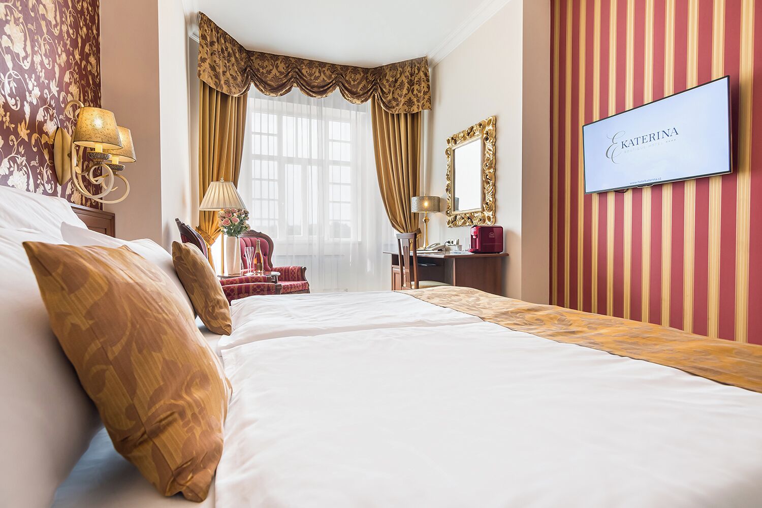 Quarto de hotel com uma cama grande, uma escrivaninha com cadeira, toucador com espelho e televisão na parede.