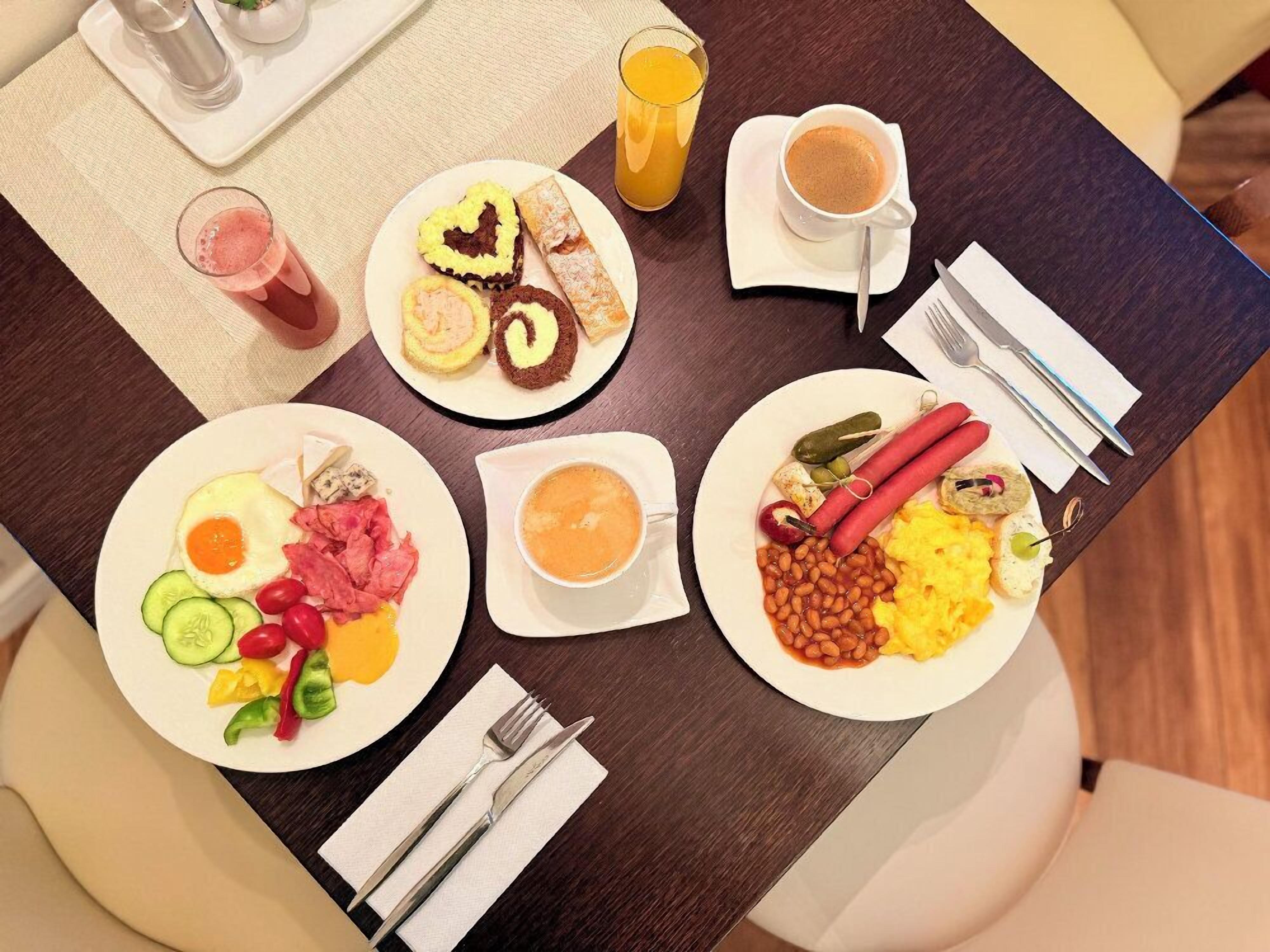Una mesa de desayuno con platos de comida, un vaso de jugo de naranja, una taza de café y cubiertos.