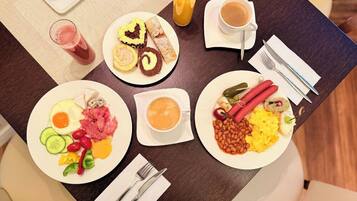 A breakfast table with plates of food, a glass of orange juice, a cup of coffee, and cutlery.