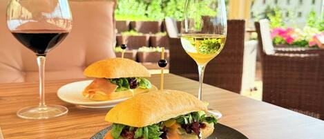 Un sándwich sobre un plato negro con dos copas de vino sobre la mesa.