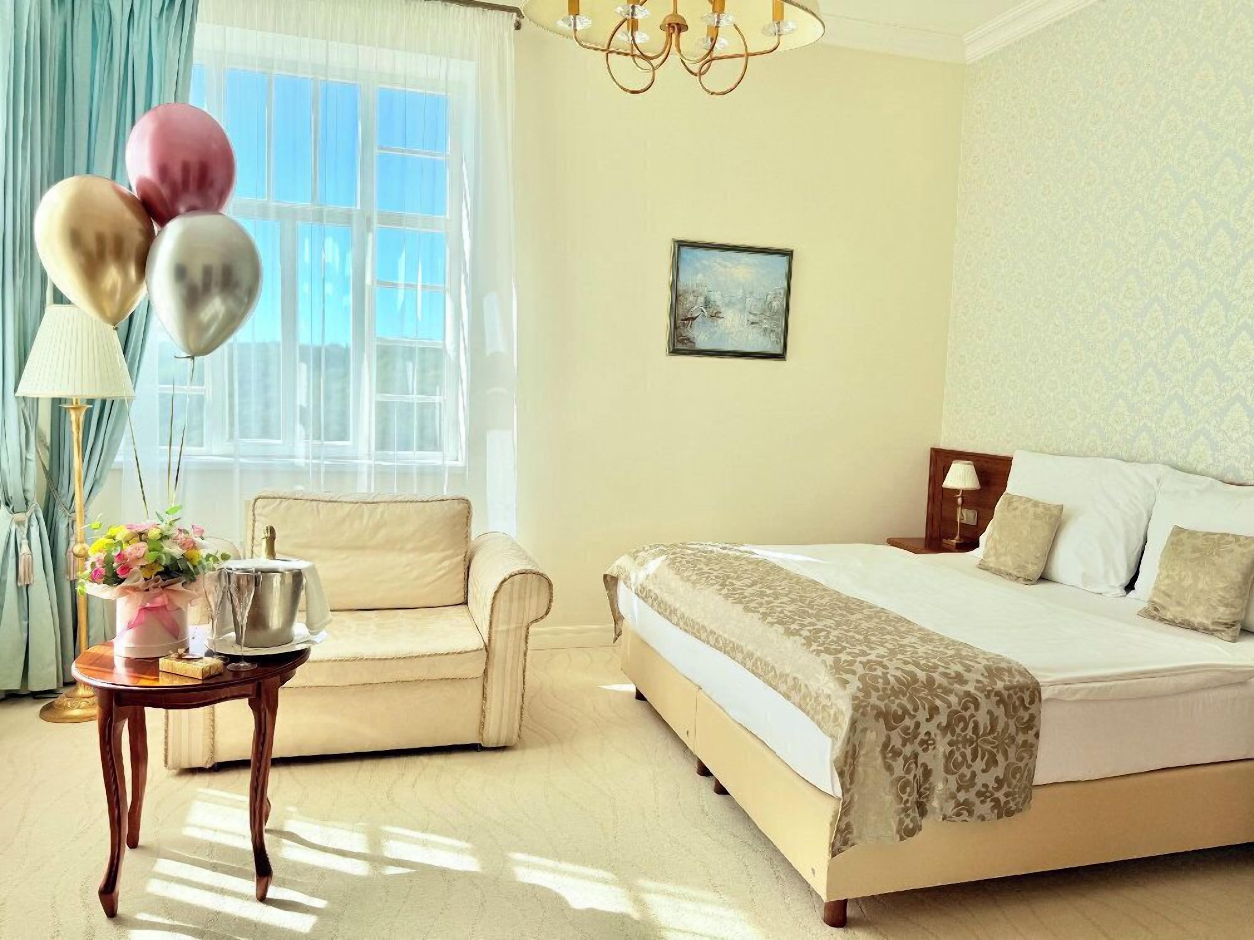 Ein Hotelzimmer mit Bett, einem Sessel, einem Tisch mit Ballons und einem Bild an der Wand.