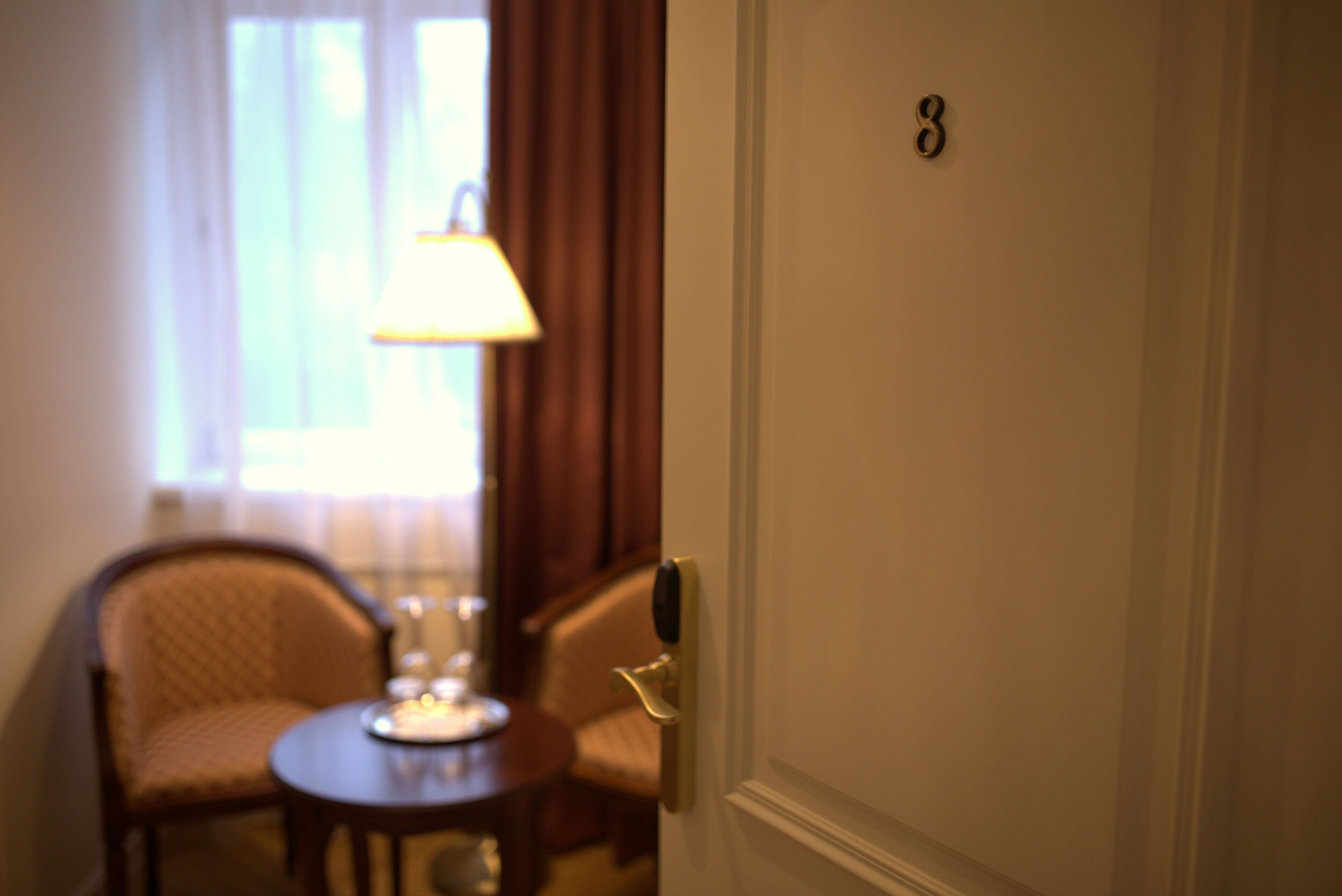 Habitación de hotel con una puerta numerada con el 8, una mesita redonda con una lámpara y dos sillas.