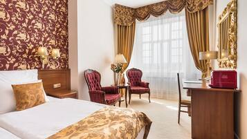 Una habitación de hotel con una cama, dos sillones rojos, un escritorio, una lámpara y un espejo.