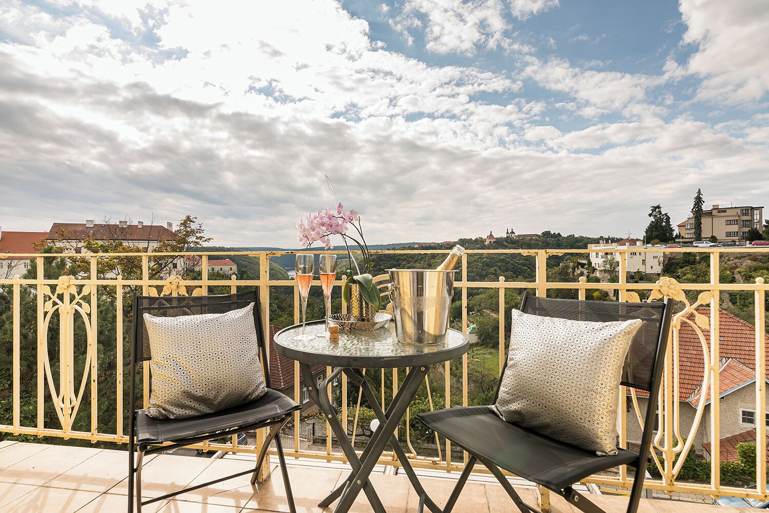 A balcony with two chairs, a table, and a vase with flowers.