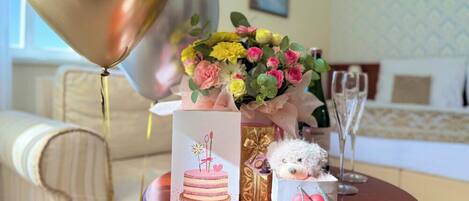 A table with a bouquet of flowers, a teddy bear, a cake illustration, a gift box, and a champagne glass.