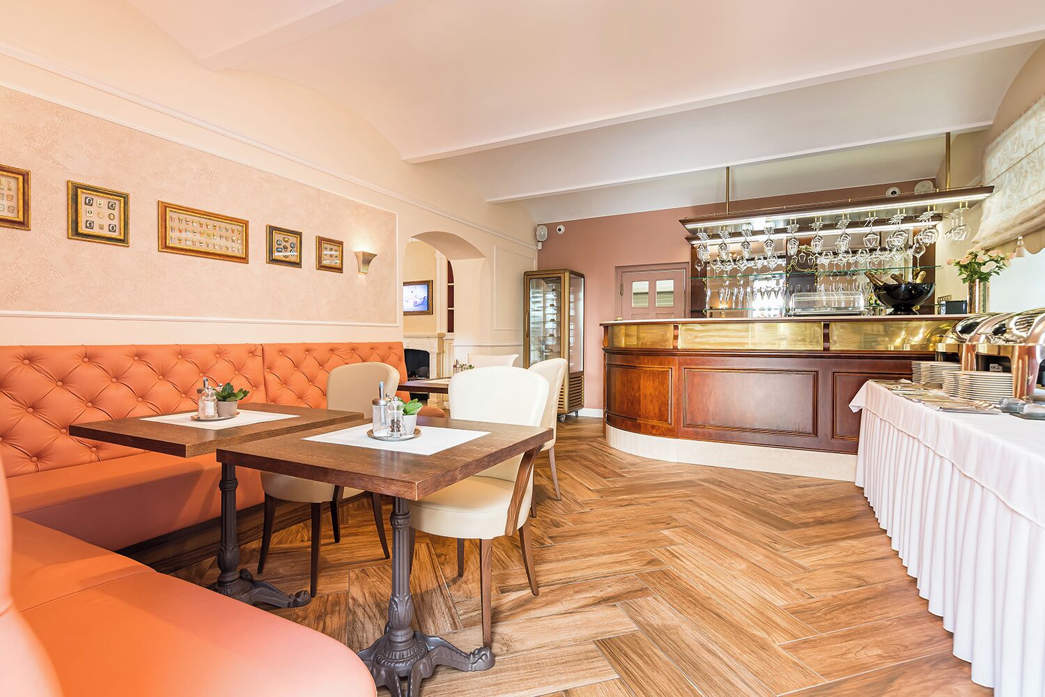 Un comedor con barra, piso de madera y una disposición de asientos que incluye un sofá naranja con capitoné y una mesa con sillas.