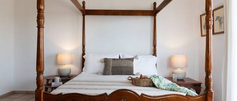 A four-poster bed with a wooden headboard, two bedside tables with lamps, and a bedside basket.