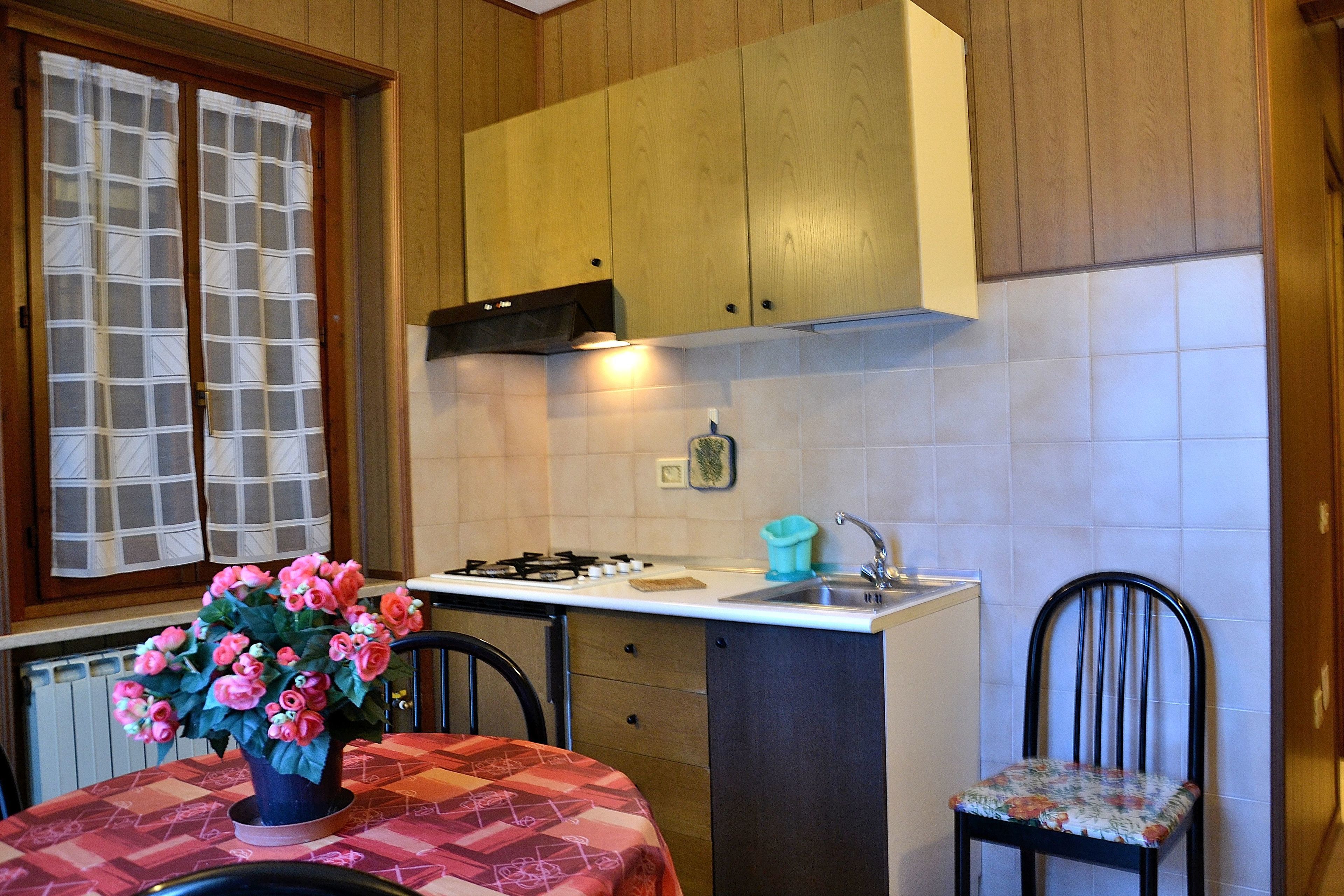 Une cuisine avec des meubles de rangement en bois, une cuisinière à gaz, un évier et une chaise.